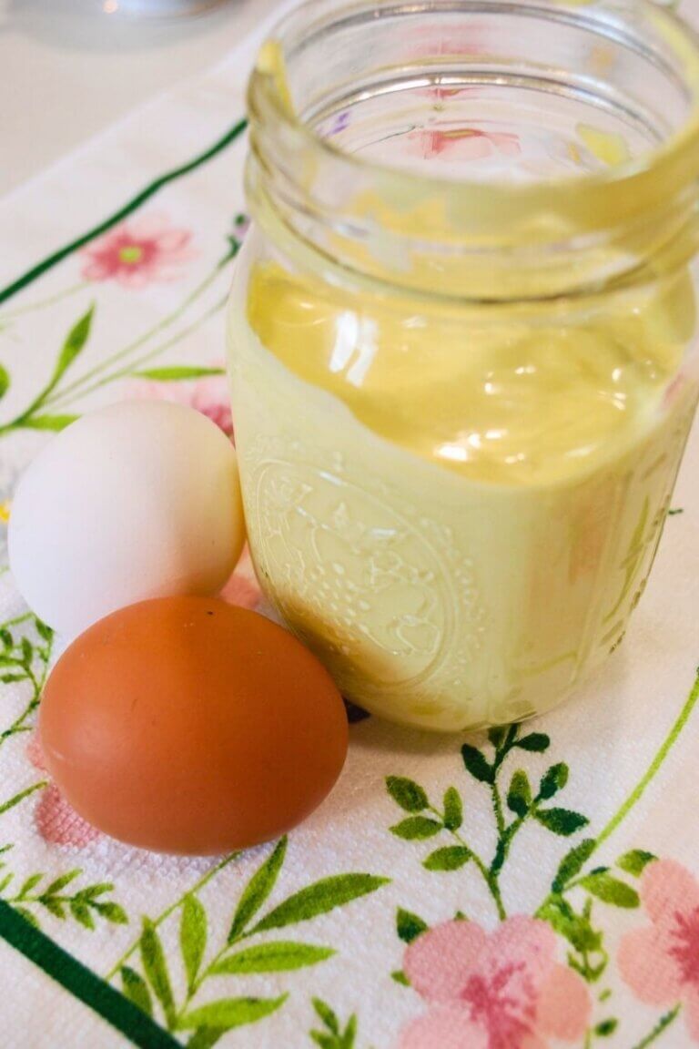Homemade mayonnaise in a mason jar with farm fresh eggs on a floral kitchen towel