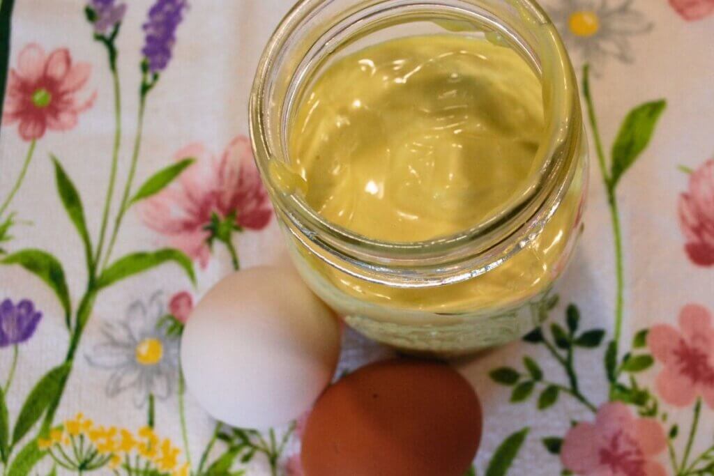 Jar of homemade avocado oil mayonnaise with brown and white eggs beside it