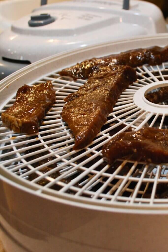 Sliced beef arranged in a single layer on dehydrator trays before drying into homemade beef jerky.