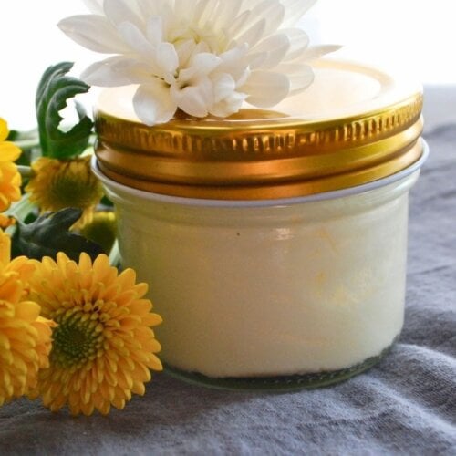 Homemade beef tallow lotion with calendula in a glass jar surrounded by flowers
