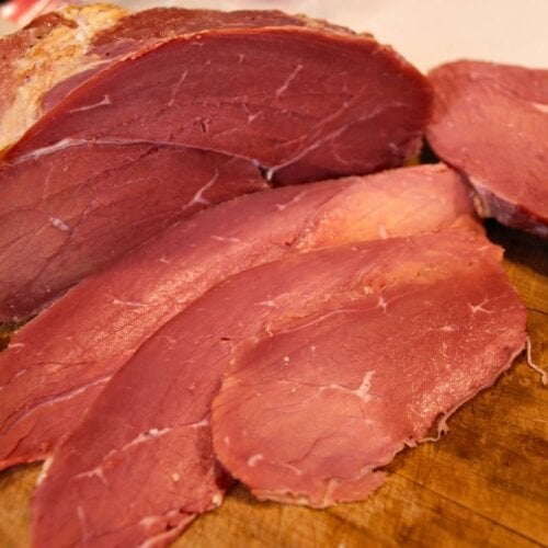 Thinly sliced homemade cured roast beef on a cutting board for deli-style sandwiches