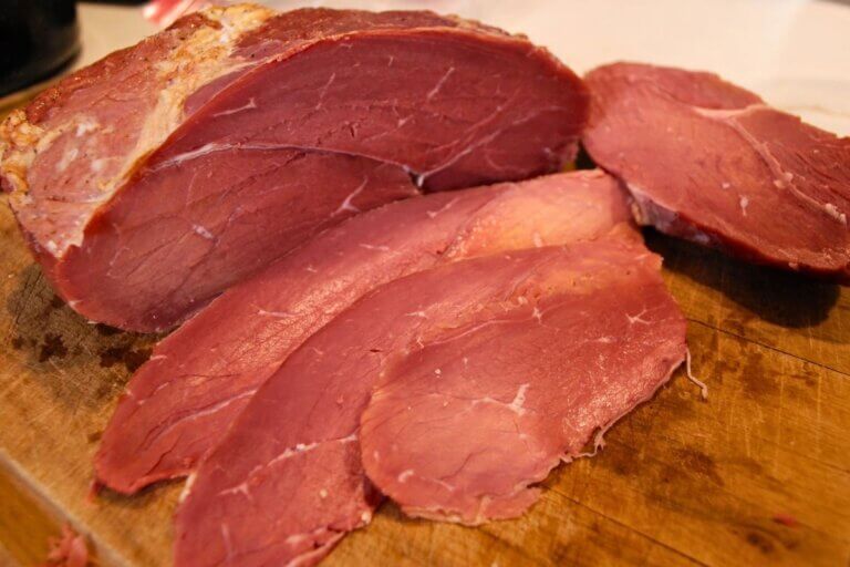 Thinly sliced homemade cured roast beef on a cutting board for deli-style sandwiches
