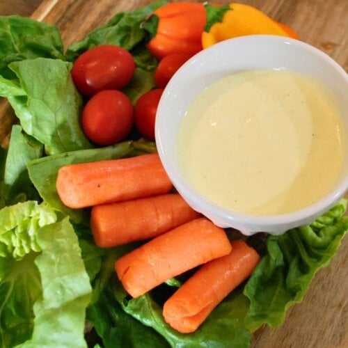 Homemade creamy garlic dip and dressing served with fresh vegetables on a wooden board.
