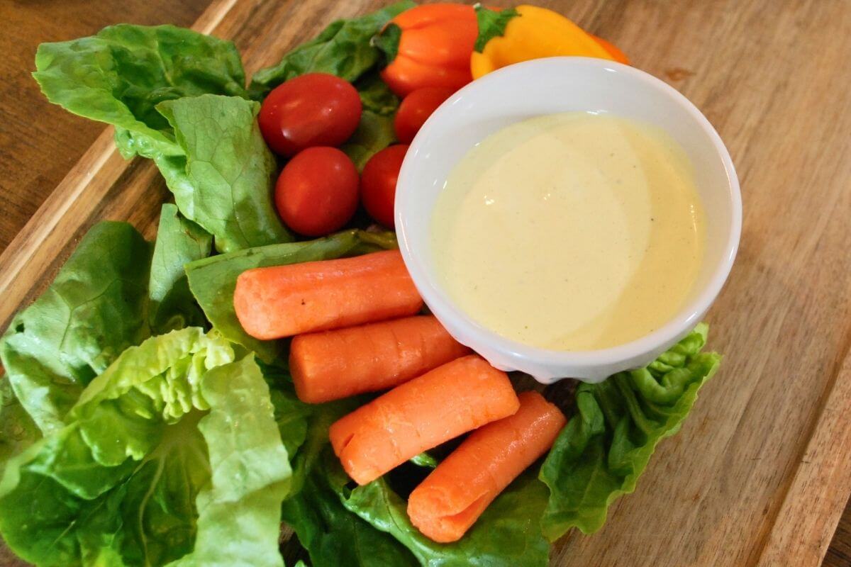 Homemade creamy garlic dip and dressing served with fresh vegetables on a wooden board.